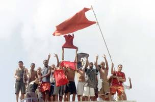 Brasil, Rio de Janeiro, RJ, 19/04/2002 Rebelião de presos na Casa de Custódia Jorge Sant'ana, em Bangu. Presos no telhado fazendo agito com a bandeira da facção Comando Vermelho (CV) (Foto: Carlos Moraes/ Agência O Dia)