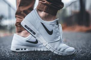 Pessoa vestindo tênis de corrida Nike branco em pé no caminho de concreto preto (Foto: unsplash.com)